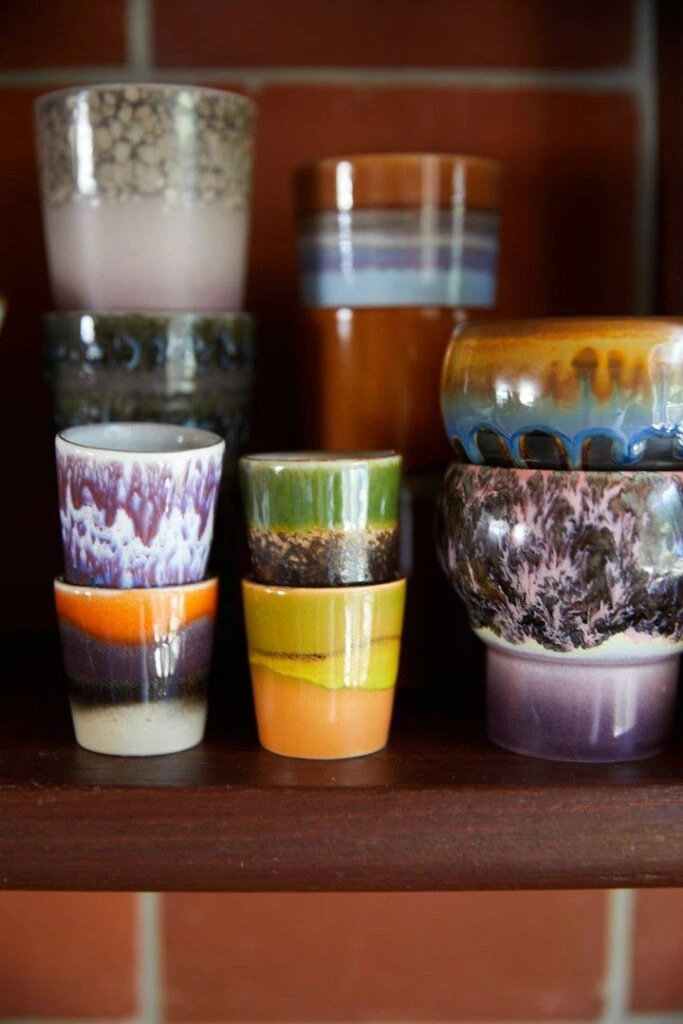 A close-up shot of a collection of stacked, multicolored ceramic mugs.