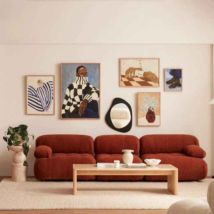 Photo of a living room featuring a terracotta-colored modular sofa, a light wood coffee table, and a gallery wall with various framed art prints.