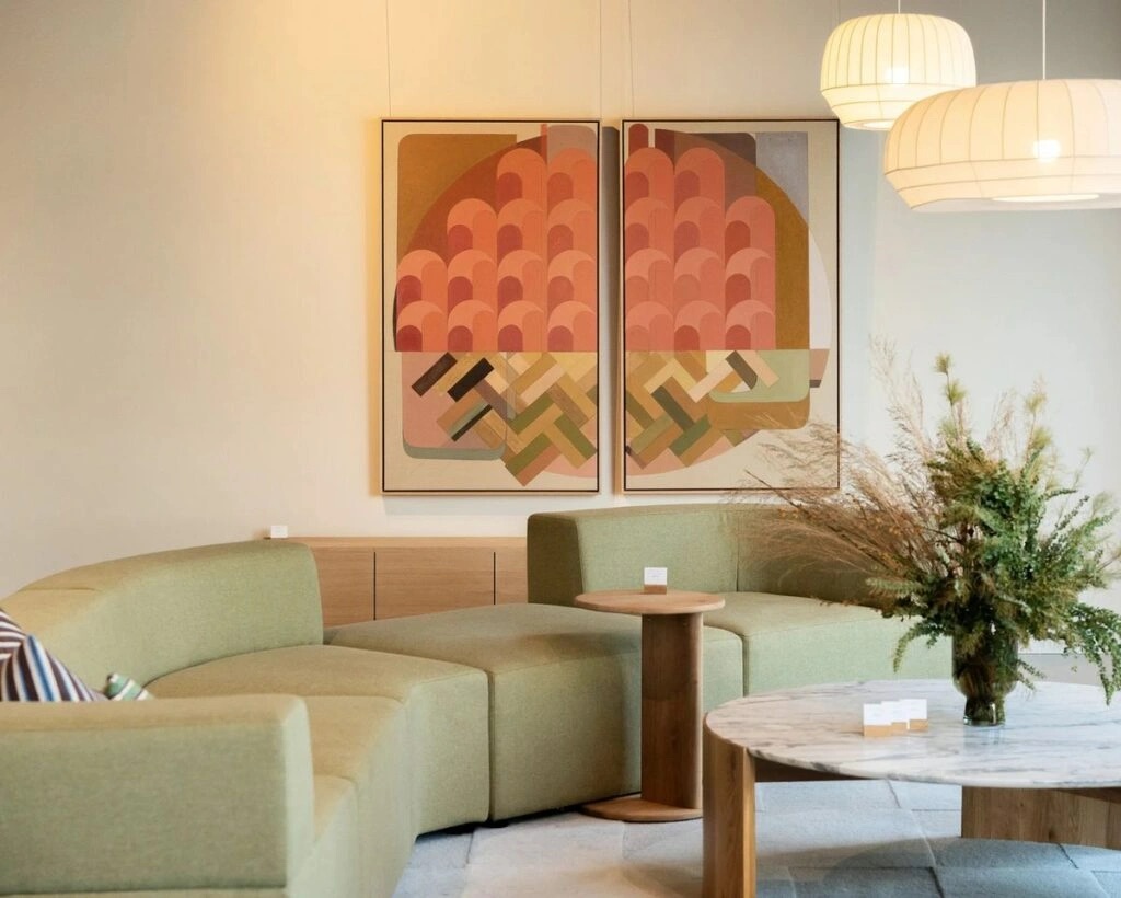 A modern lounge area with a curved green sofa, an abstract painting on the wall, and a marble coffee table with a dried floral arrangement.