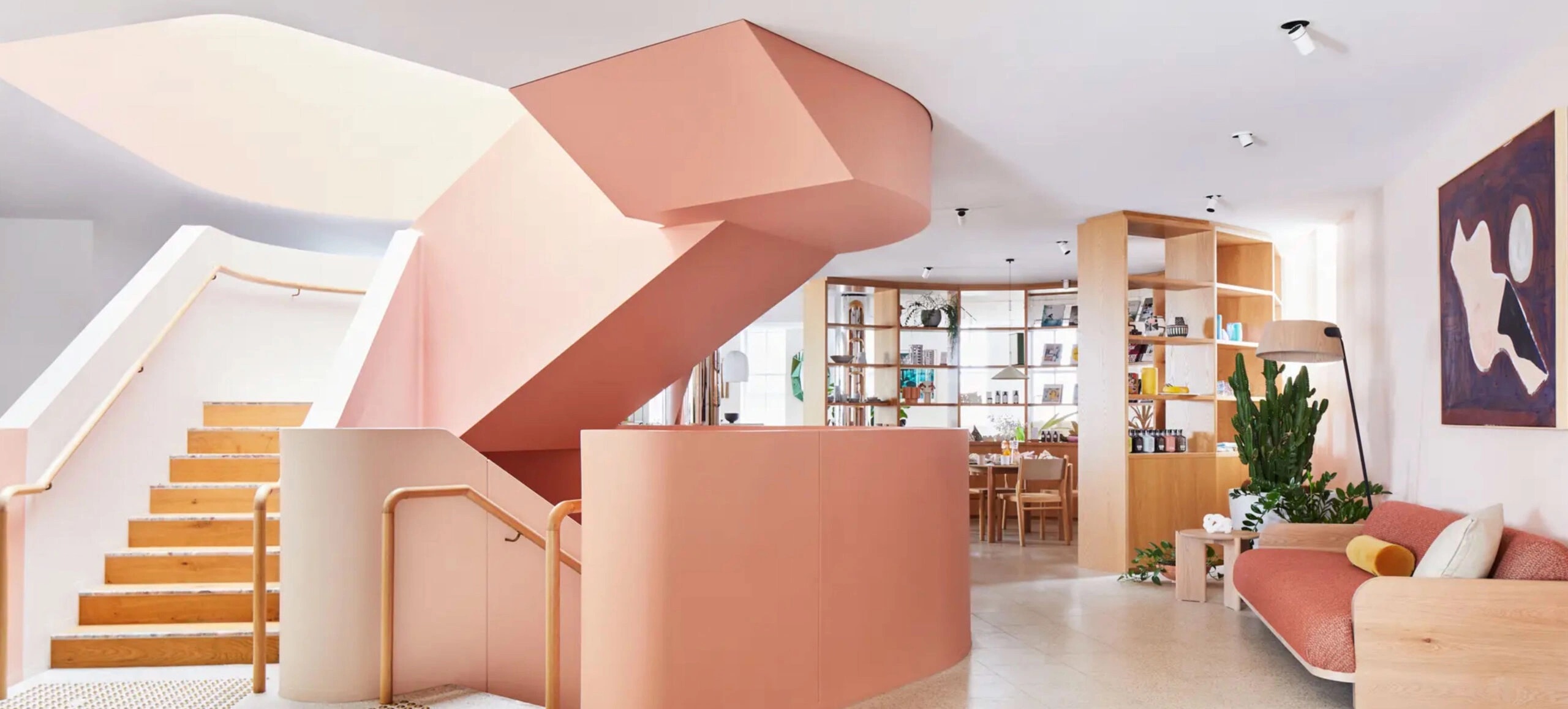 A modern interior space with a large, curved pink staircase, wooden steps, and minimalist furniture.