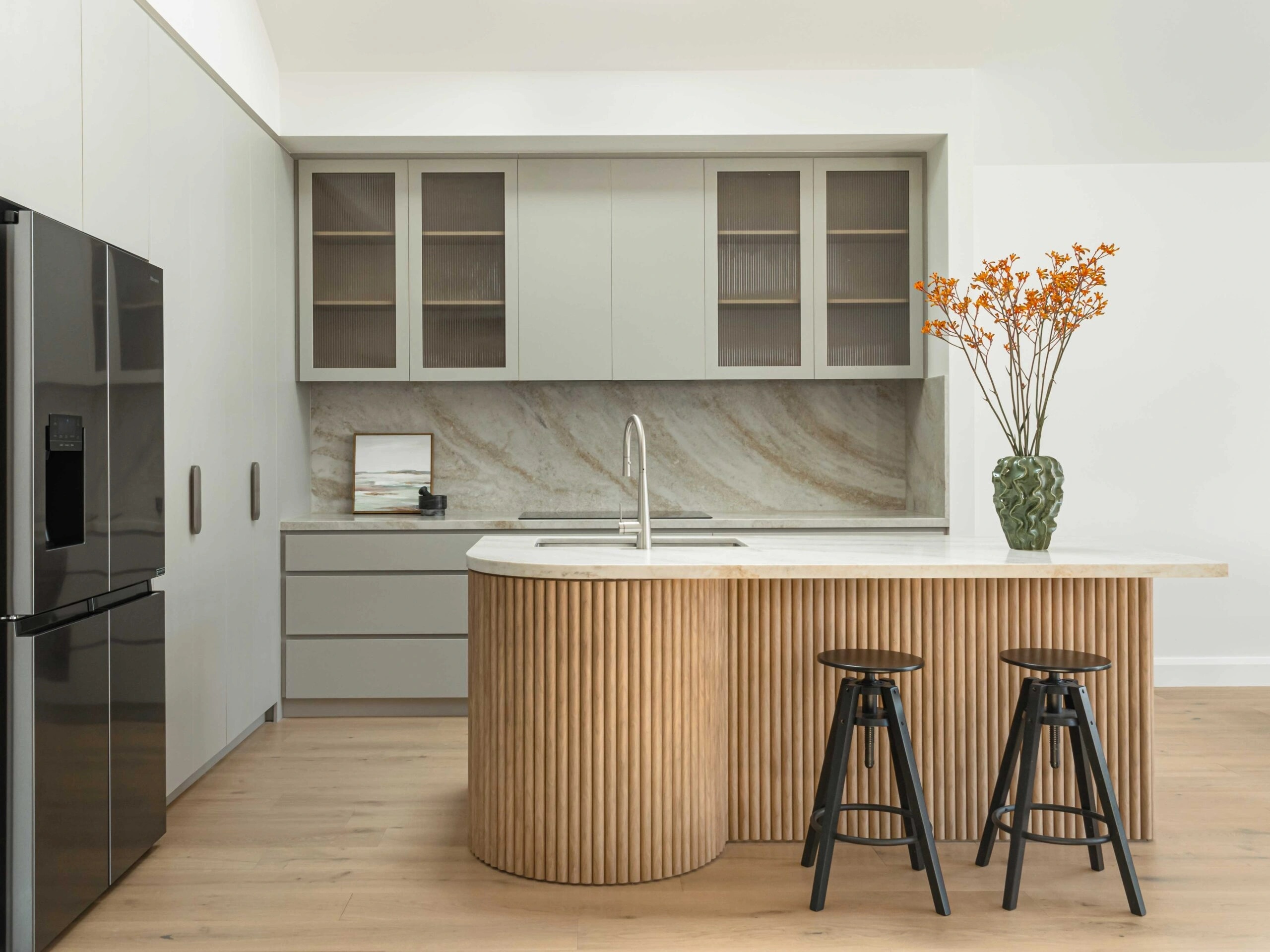 A modern kitchen featuring a fluted wooden island, a marble backsplash, and light-coloured cabinetry.
